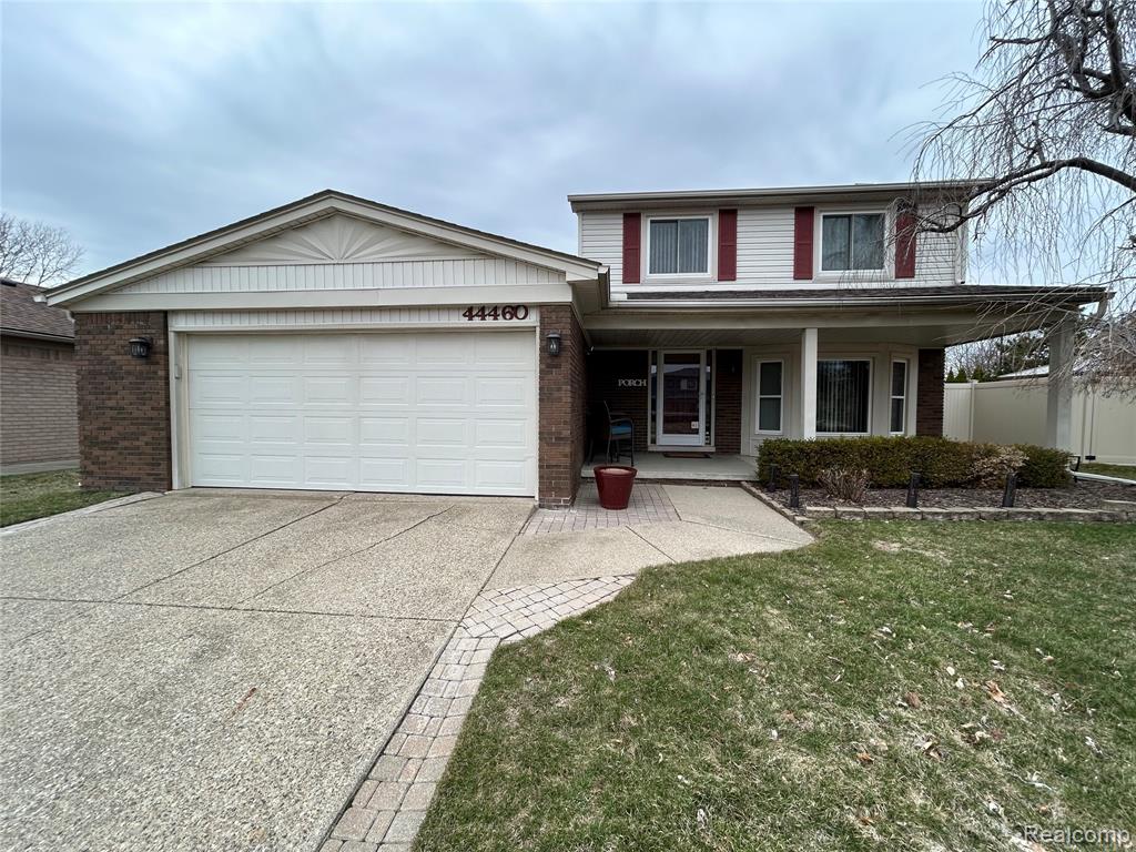 Traditional-style house with a porch, an attached garage, concrete driveway, and brick siding