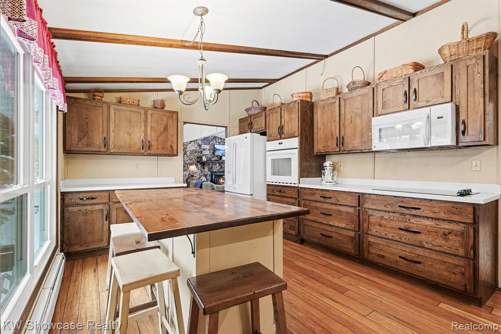 Kitchen featuring butcher block countertops, a breakfast bar, vaulted ceiling with beams, a chandelier, and white appliances