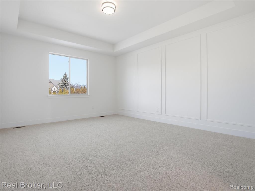 Empty room featuring a tray ceiling, light carpet, and a decorative wall
