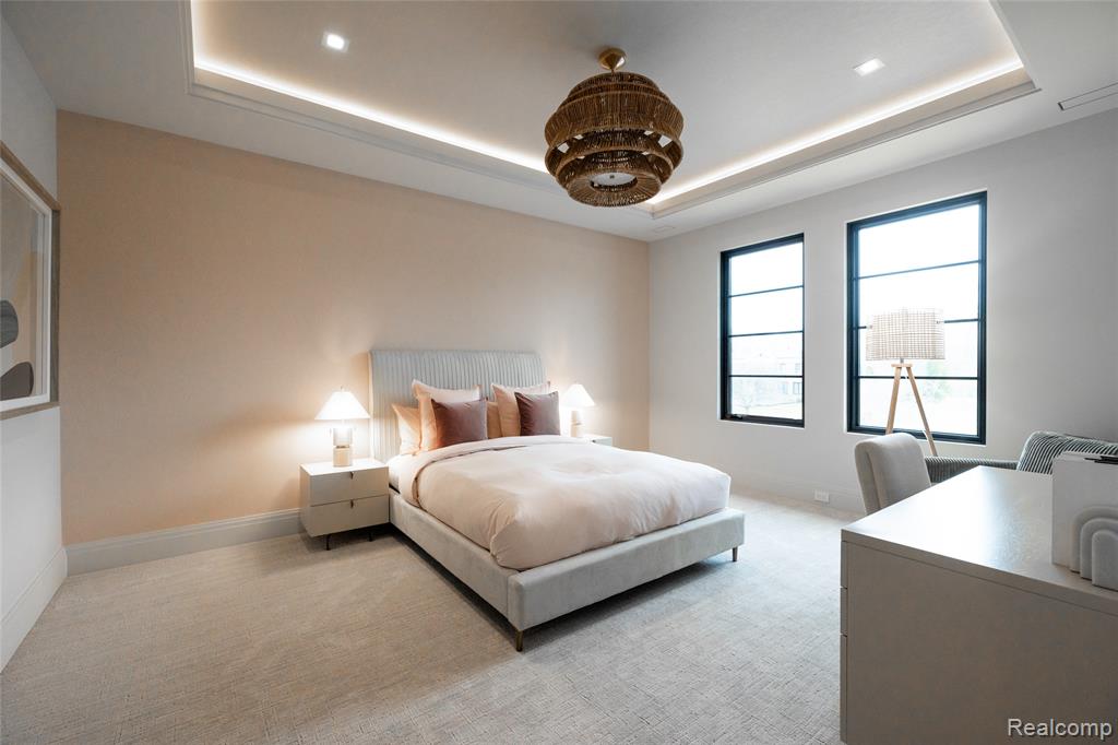Bedroom with a tray ceiling, light colored carpet, and a desk