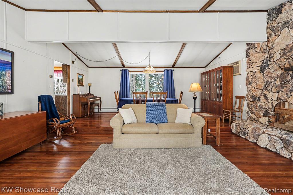 Living room with dark wood finished floors, hanging lights, vaulted ceiling with beams, and a baseboard radiator