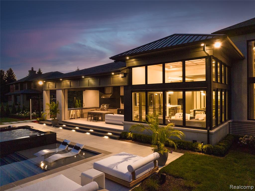 Back of property at dusk with a jacuzzi, an outdoor pool, a patio, and a metal roof