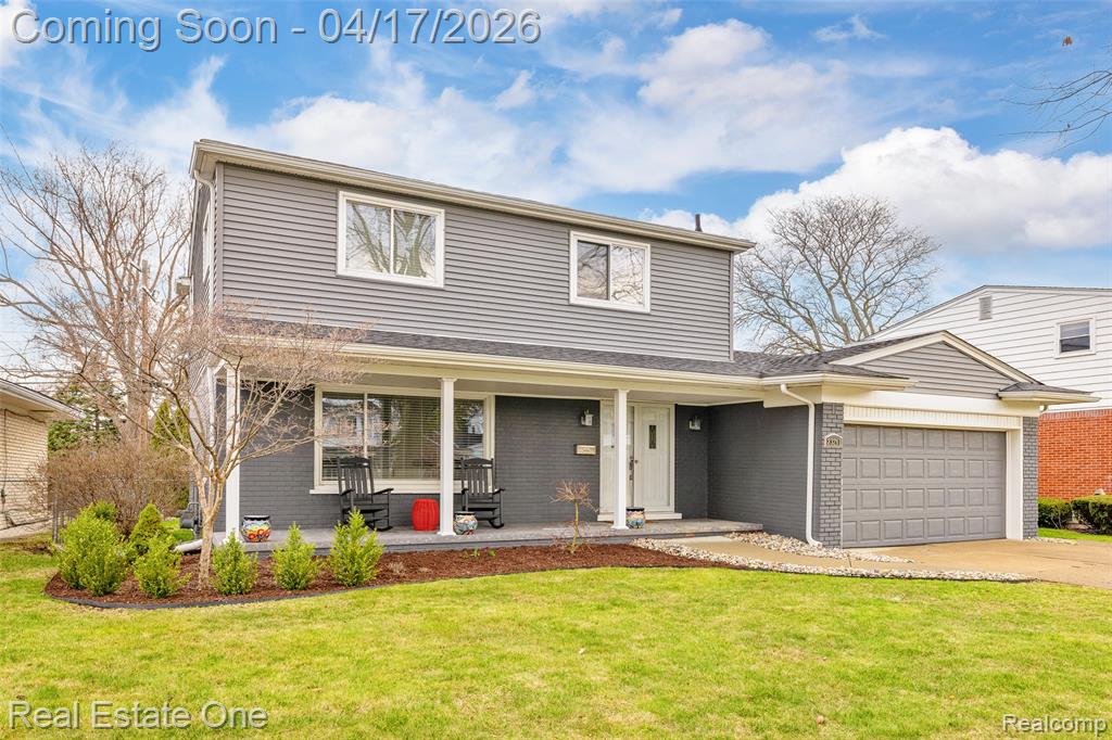 Traditional home with a front yard, an attached garage, brick siding, and covered porch