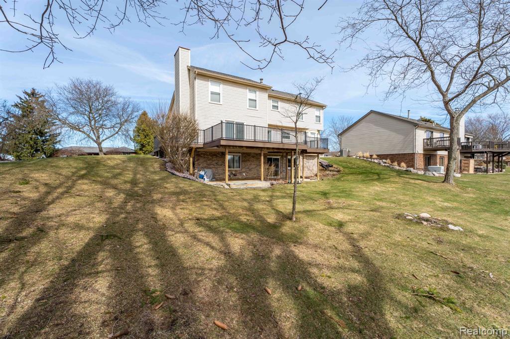 Back of property with a wooden deck, a patio area, a chimney, and a yard