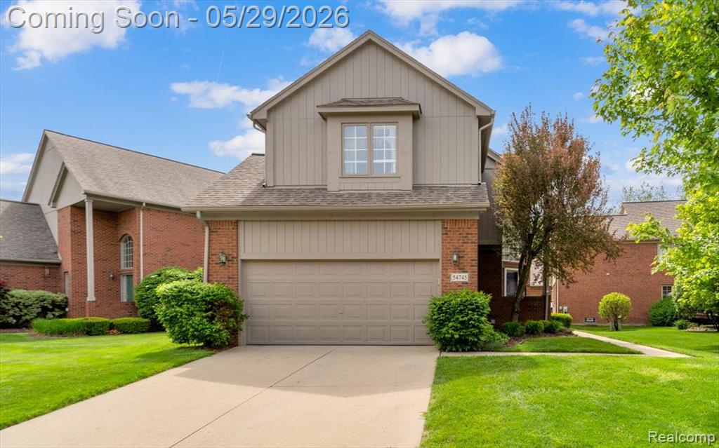 View of front facade featuring a front yard, driveway, a shingled roof, and an attached garage