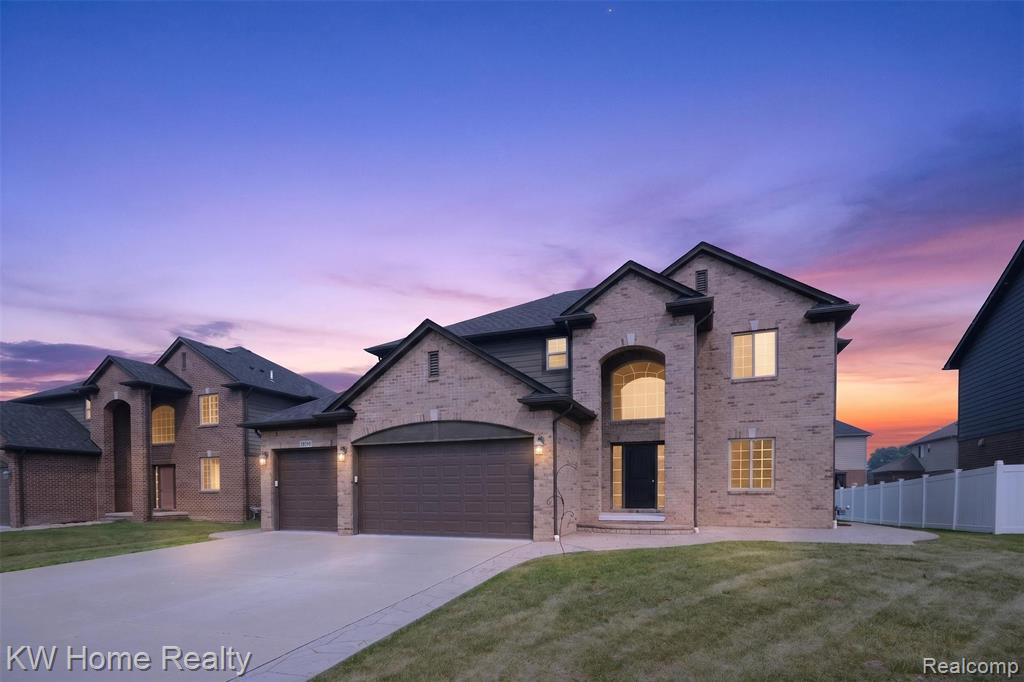Brick exterior with arched window accents, dark asphalt shingle roof, attached garage with twin doors, concrete driveway, and a manicured lawn