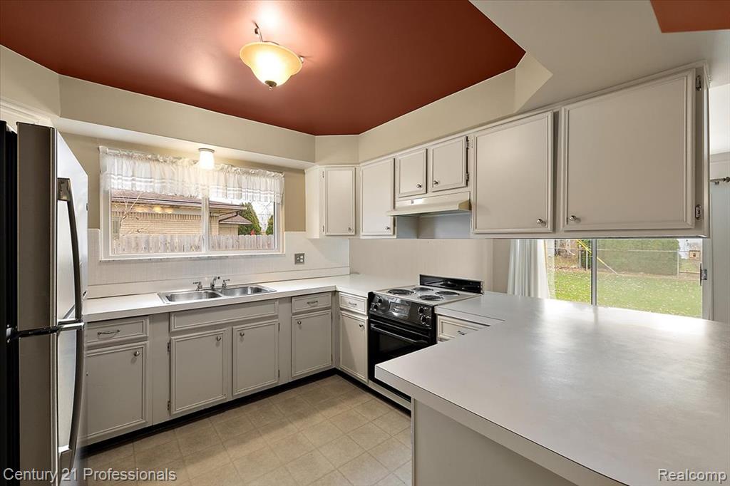 Kitchen with freestanding refrigerator, electric range oven, light countertops, and a peninsula