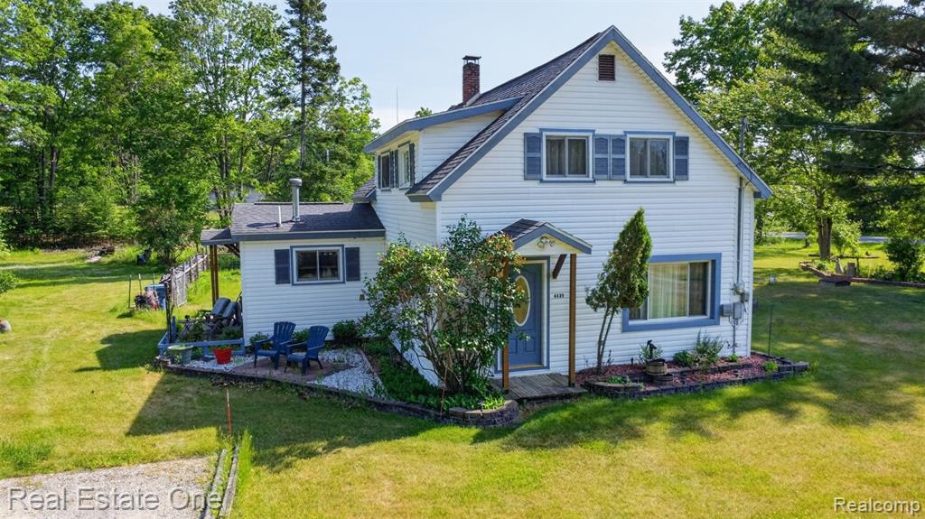 White siding exterior with blue trim and shutters, covered front entry, established landscaping, attached back patio, and expansive surrounding green space