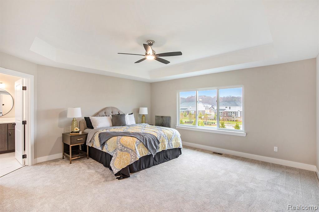 Bedroom with a tray ceiling, ensuite bath, carpet floors, and a ceiling fan