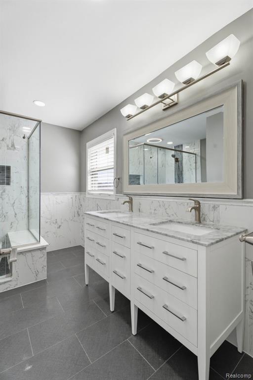 Bathroom with double vanity, tile walls, a wainscoted wall, a marble finish shower, and dark tile patterned flooring