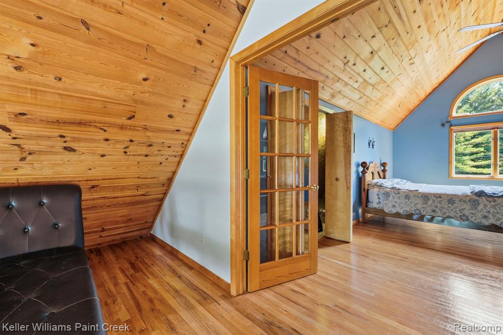 Slanted wood-paneled wall, wood-paneled ceiling, wood-finish flooring, French doors with multiple glass panes, arched window with wood trim