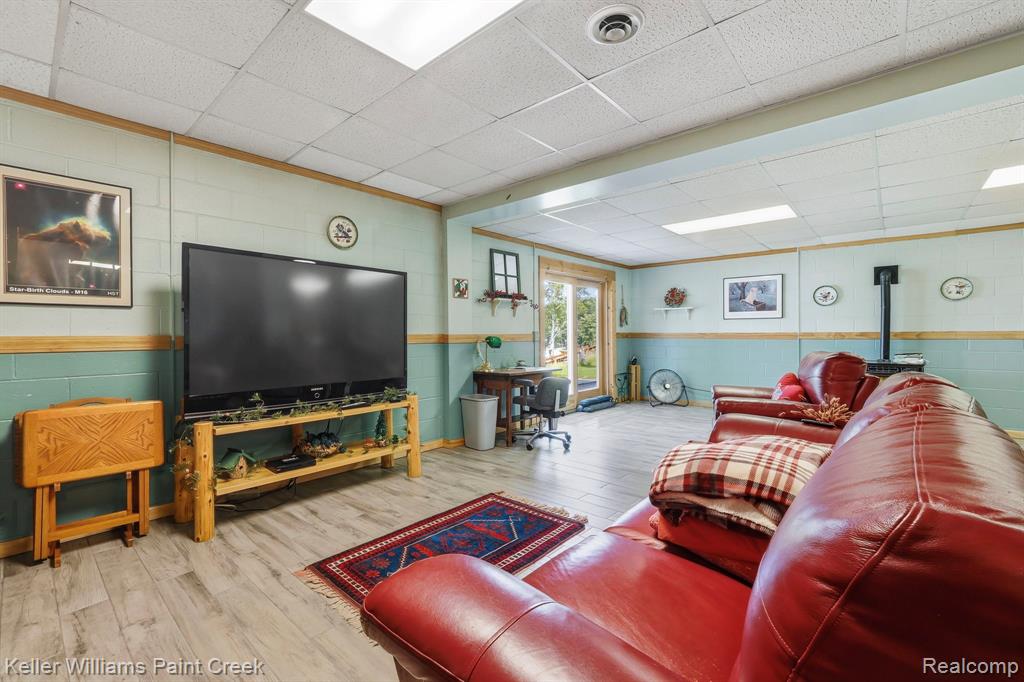 Wood-finish flooring, drop ceiling with recessed lighting, wainscoting, and a built-in wood stove
