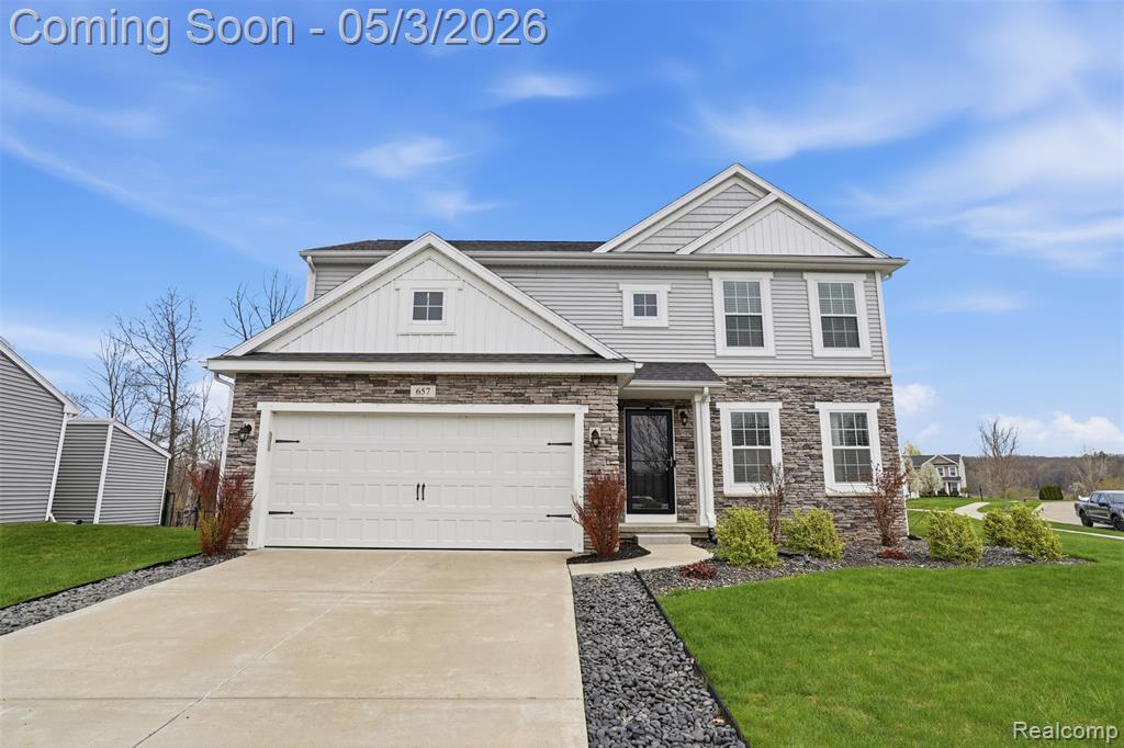View of front of house with stone siding, a front yard, driveway, and board and batten siding