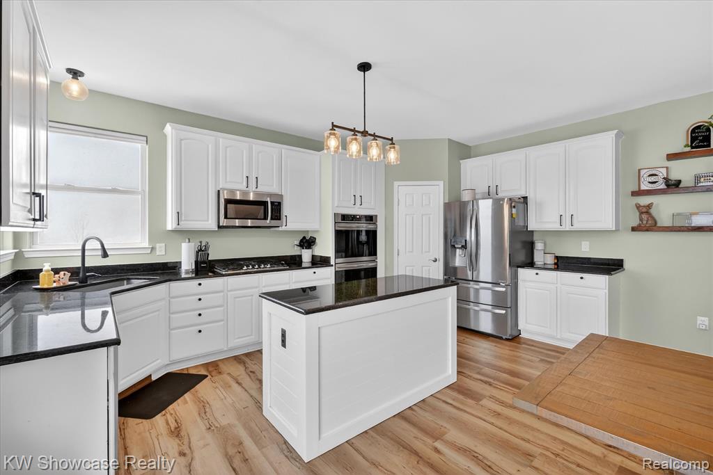 Kitchen featuring white cabinetry, stainless steel fridge, open floor plan, pendant lighting, and dark stone counters