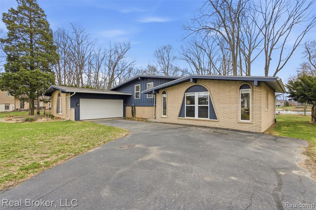 View of front facade featuring asphalt driveway, brick siding, a front yard, a garage, and board and batten siding
