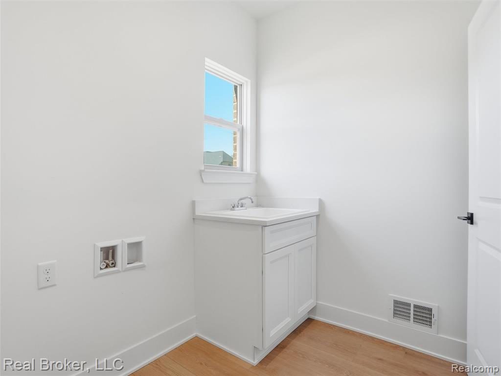Laundry room with light wood-type flooring, hookup for a washing machine, and cabinet space