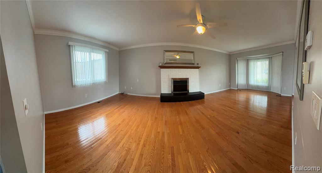 Unfurnished living room with a ceiling fan, wood finished floors, a brick fireplace, and ornamental molding