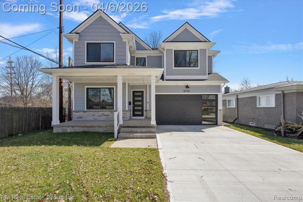 View of front of home with covered porch, concrete driveway, a garage, and stone siding