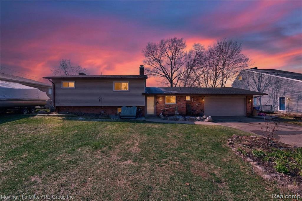 Split level home featuring an attached garage, concrete driveway, a chimney, a lawn, and brick siding