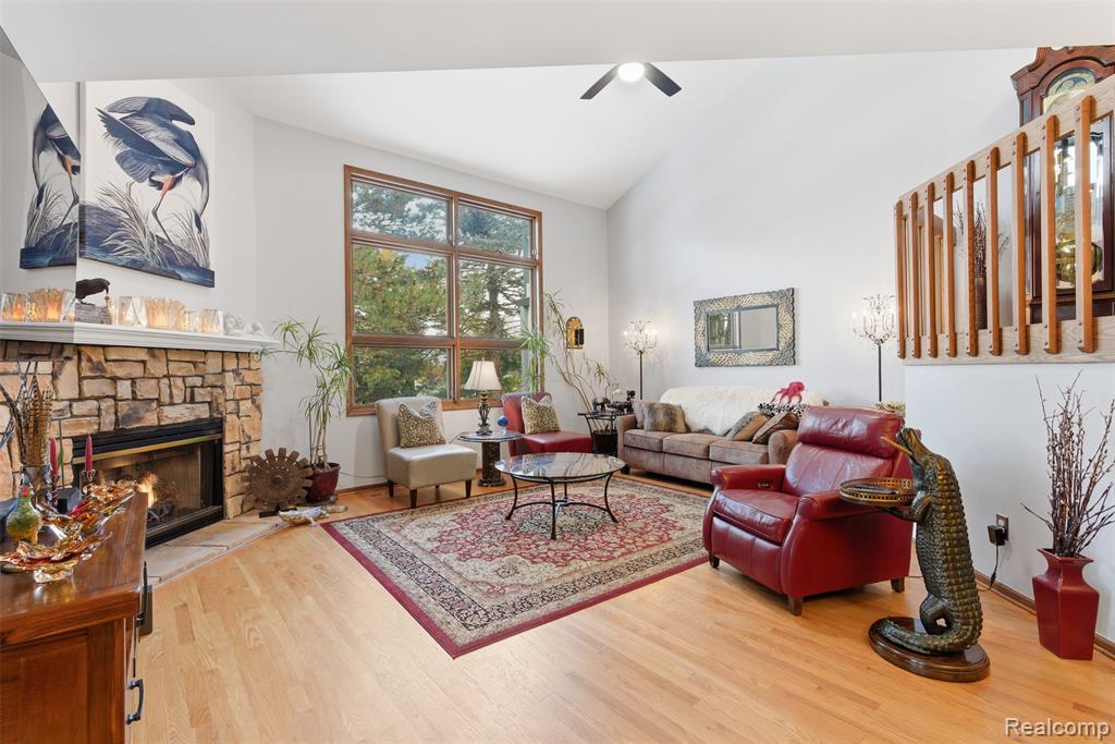 Living area with vaulted ceiling, light wood-style floors, a stone fireplace, and ceiling fan