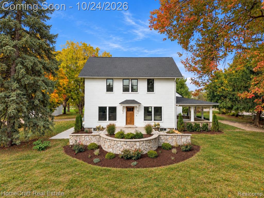 Two-story exterior featuring white horizontal siding, a natural wood entry door, a stone-accented curved retaining wall, and a side covered porch with stone pillars