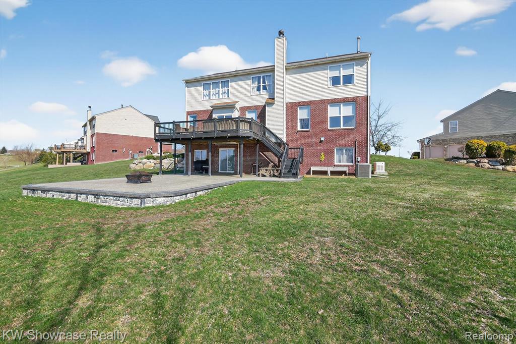 Back of house featuring a deck, a fire pit, a yard, and brick siding