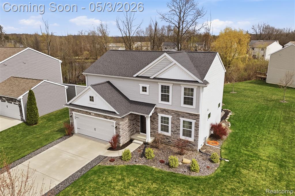 View of front of house featuring a shingled roof, a front lawn, concrete driveway, and stone siding