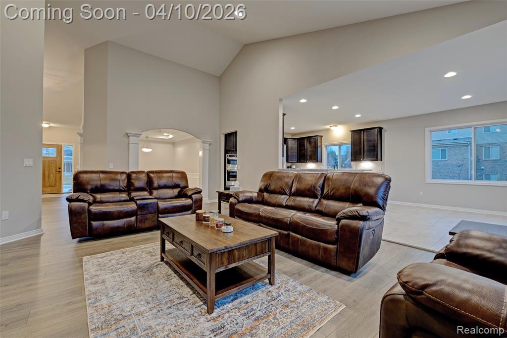 Living area featuring ornate columns, lofted ceiling, arched walkways, light wood-style flooring, and recessed lighting