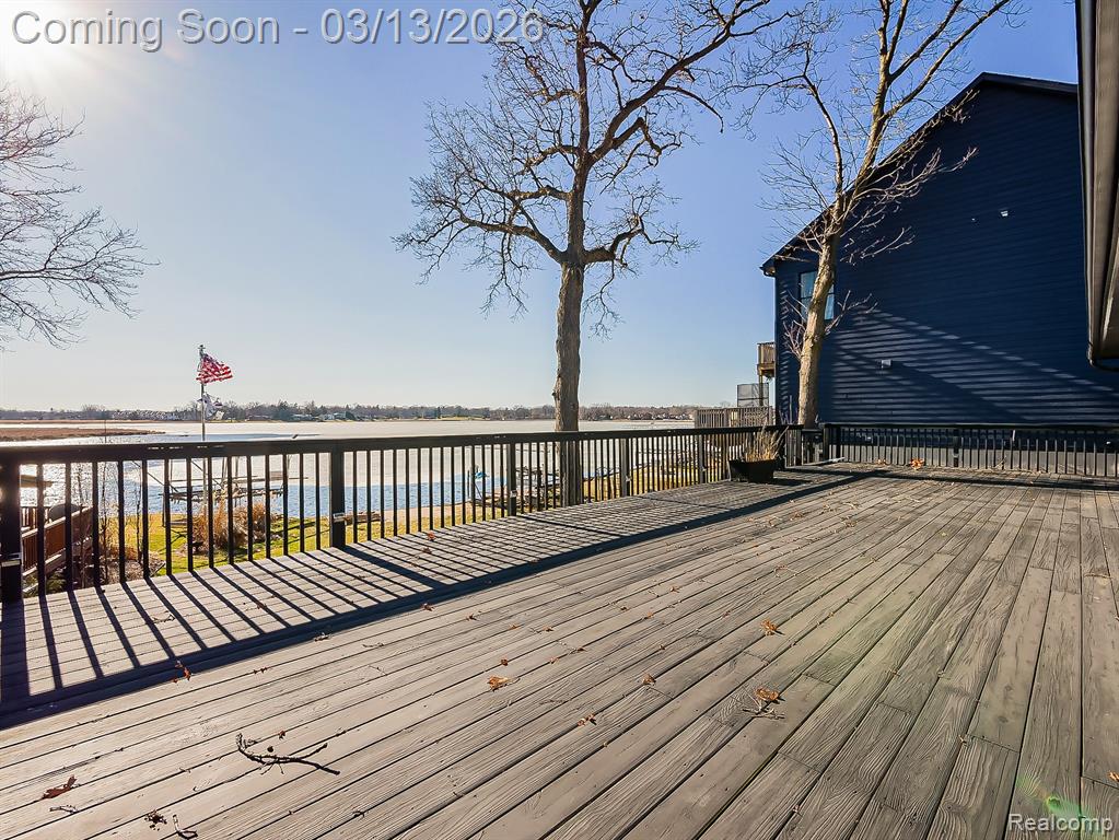 View of green lawn with boat lift, a boat dock, and a deck with water view