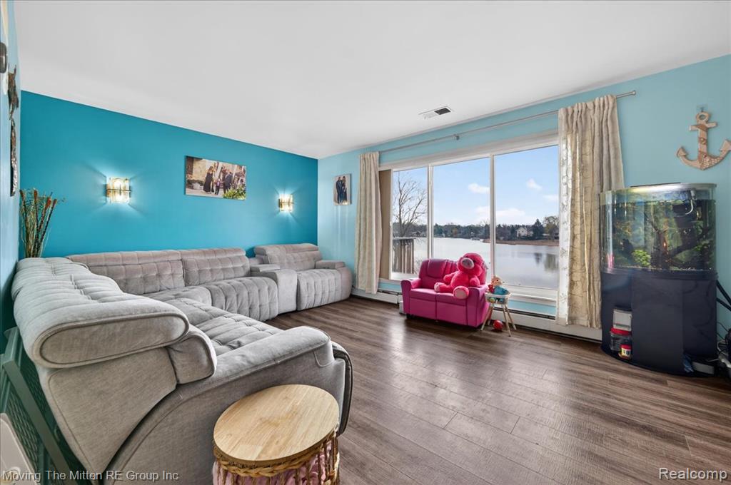 Living room with dark wood-style floors, a water view, a baseboard heating unit, and a baseboard radiator