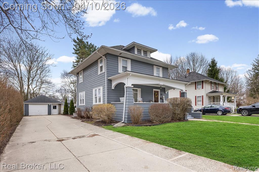 Traditional style home with covered porch, a detached garage, an outbuilding, and a front yard