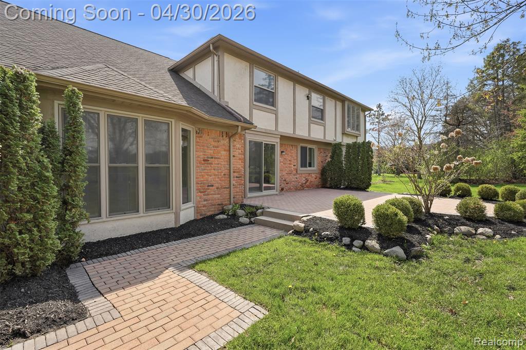 Rear view of property featuring brick siding, a yard, stucco siding, a deck, and a shingled roof