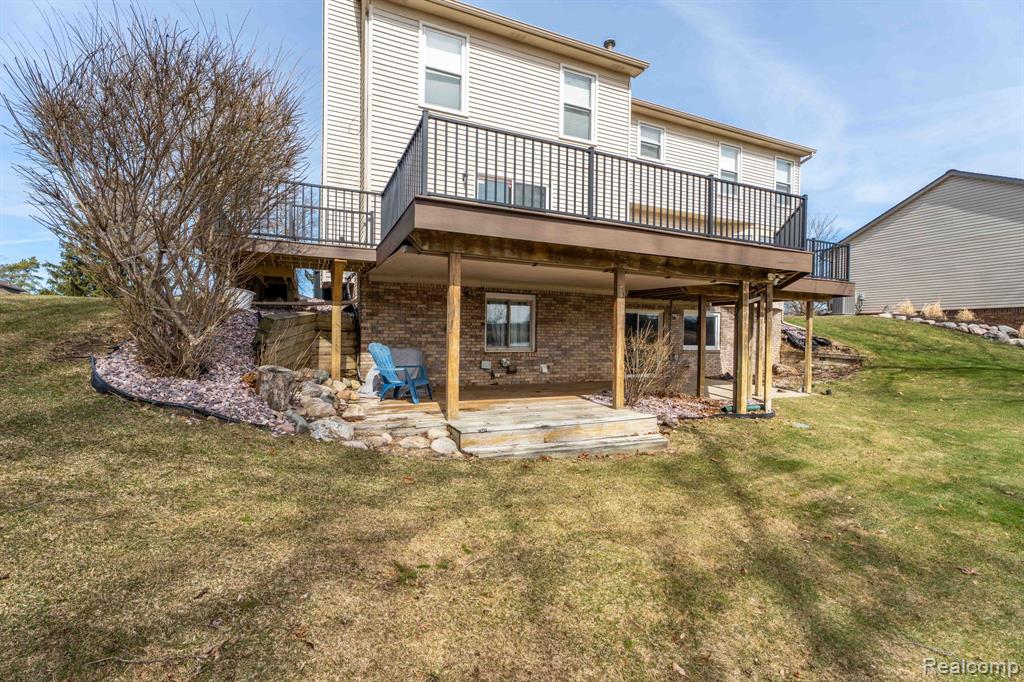 Back of property with a wooden deck, a lawn, and brick siding