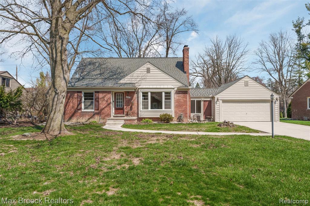 View of front of home featuring an attached garage, a front yard, brick siding, a chimney, and driveway
