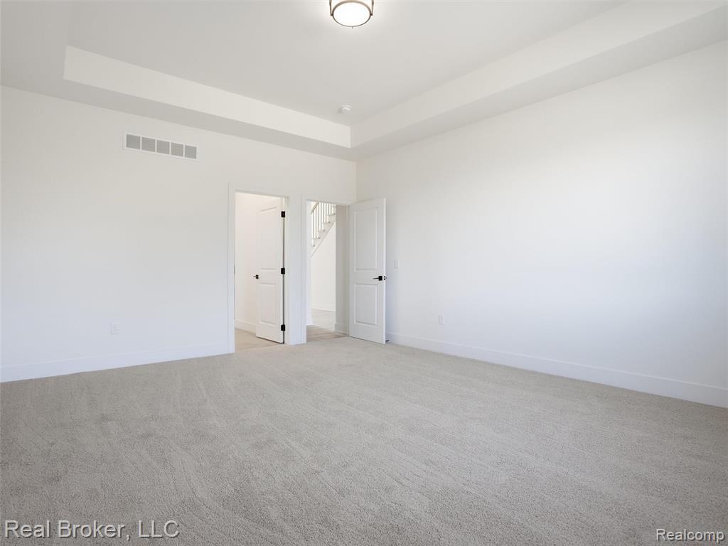 Unfurnished bedroom featuring light carpet and a tray ceiling