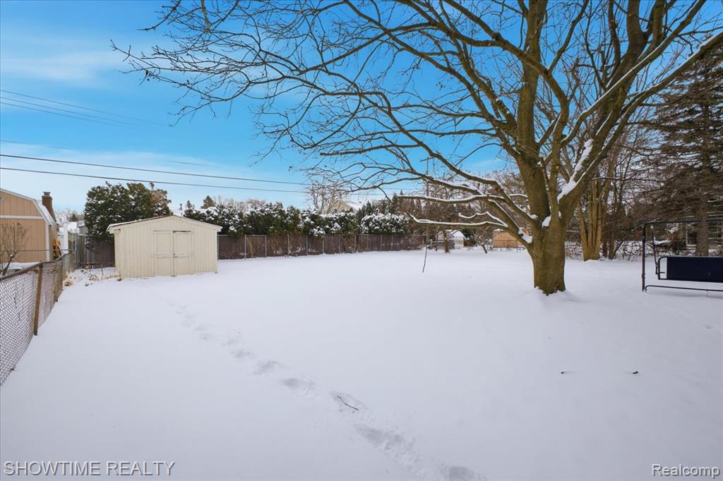 Yard layered in snow featuring a fenced backyard and a shed