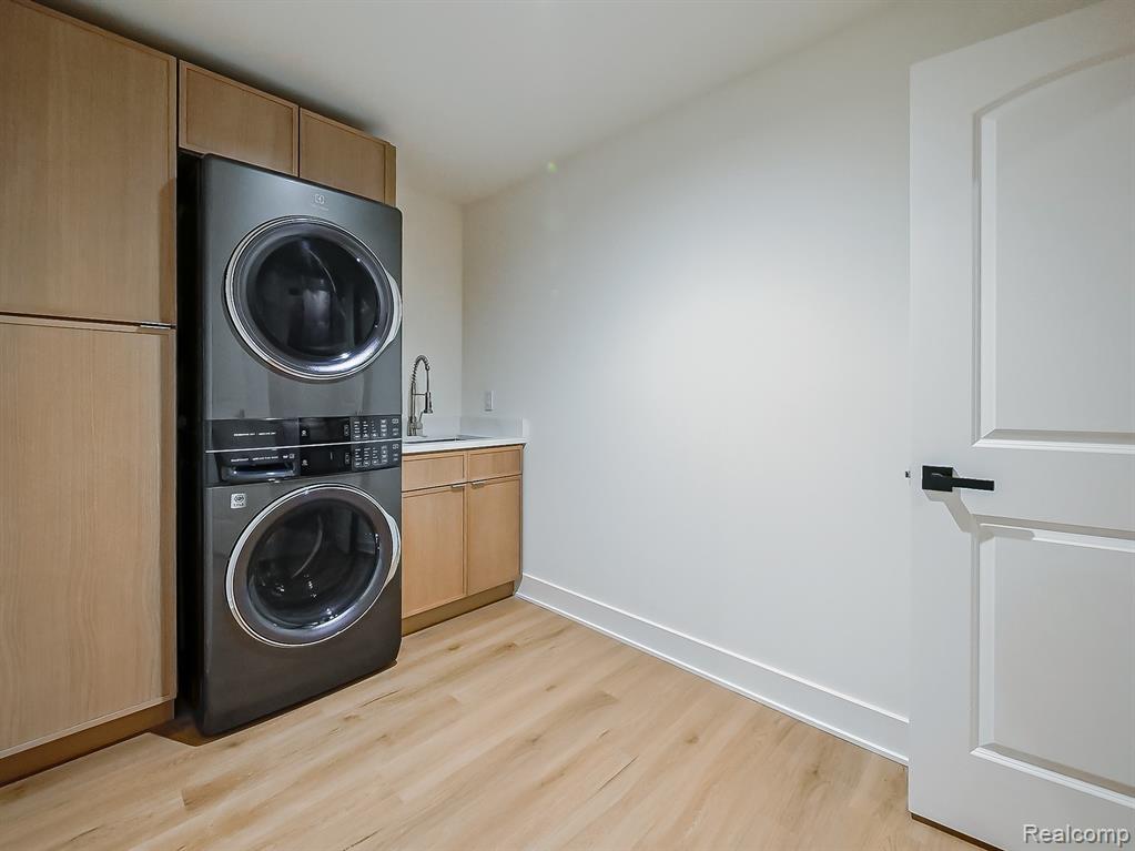 Laundry room with stacked washing machine and dryer, cabinet space, and light wood finished floors
