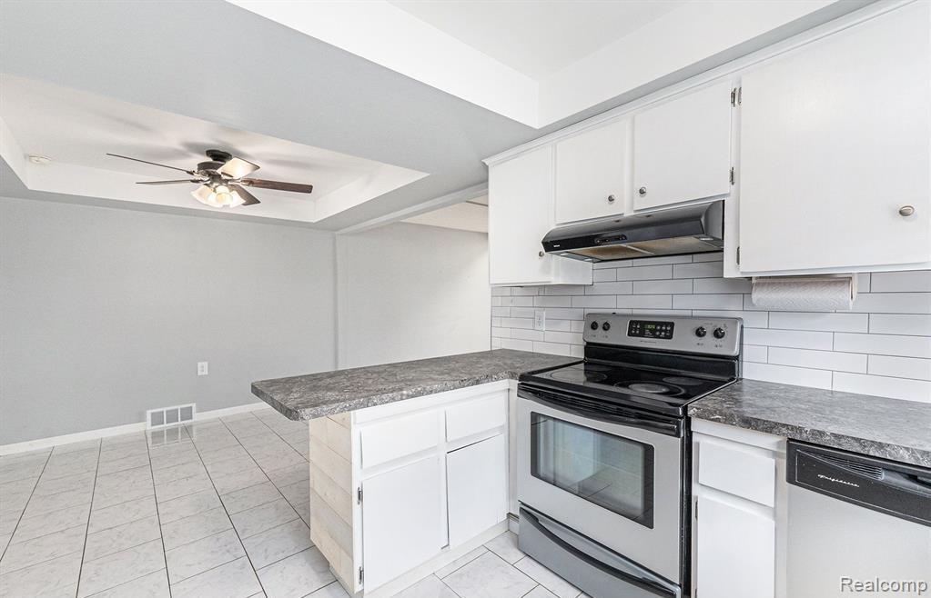 Kitchen featuring stainless steel appliances, a peninsula, a raised ceiling, and white cabinetry