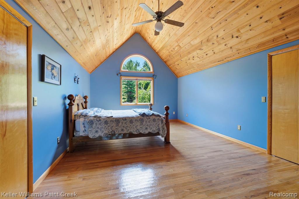 Vaulted wood-paneled ceiling, wood-finish flooring, arched window, and ceiling fan with light fixture