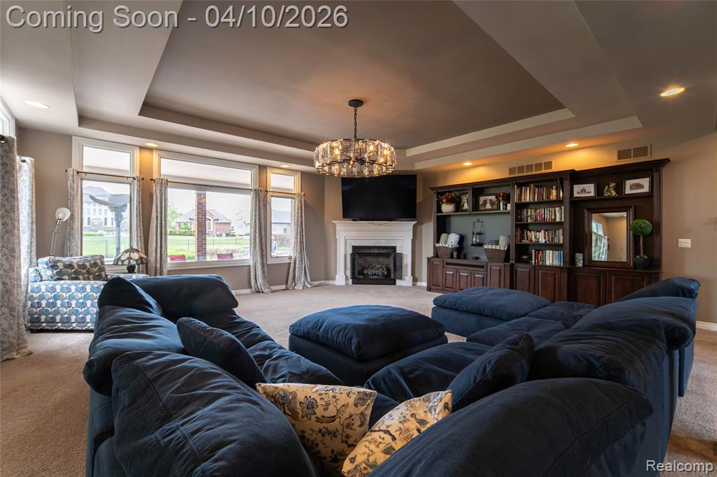 Living area with carpet, hanging lights, a tray ceiling, and a fireplace