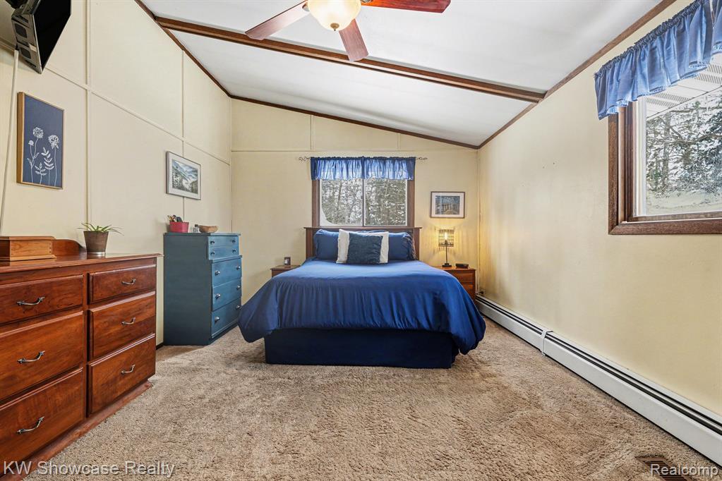 Bedroom with a baseboard heating unit, light colored carpet, lofted ceiling, and ceiling fan