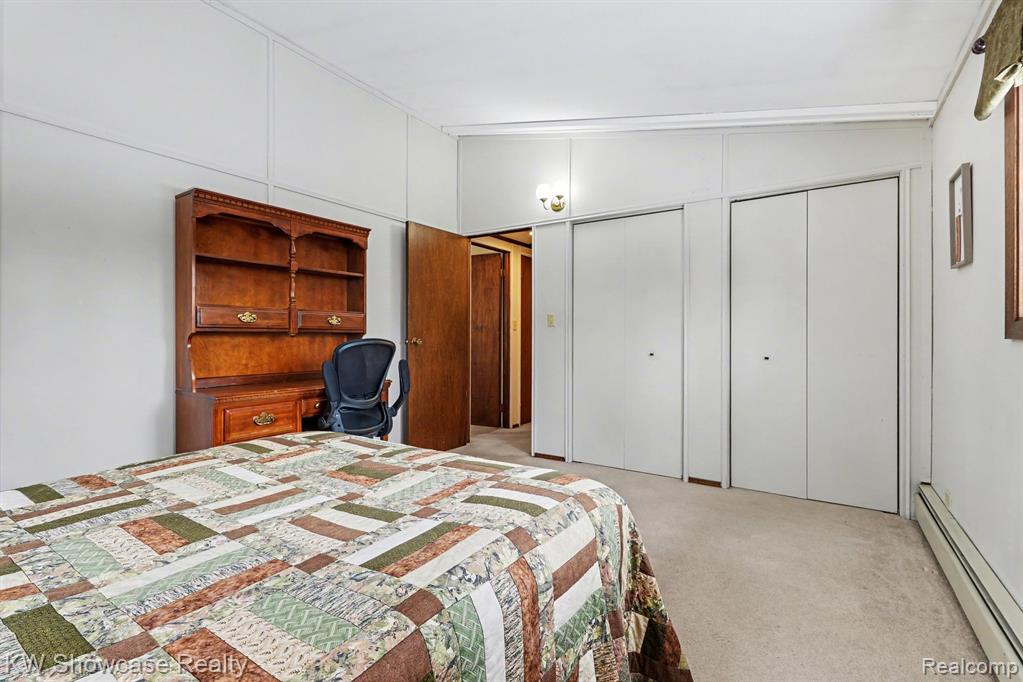 Bedroom featuring a baseboard radiator, a closet, lofted ceiling, light carpet, and a decorative wall
