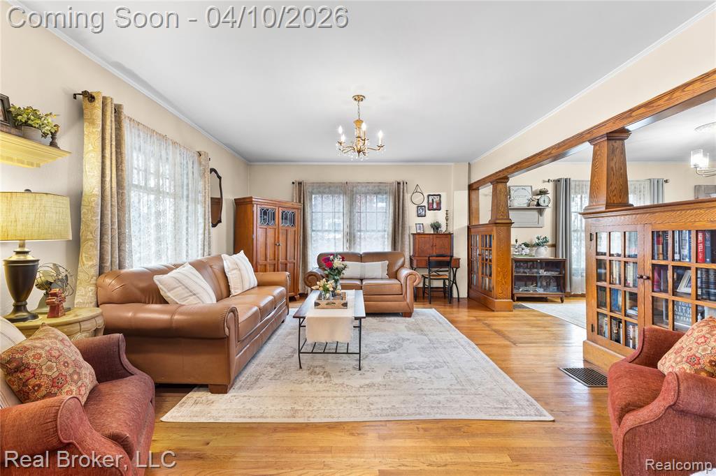 Living room with suspended lighting, light wood-style floors, plenty of natural light, and ornamental molding