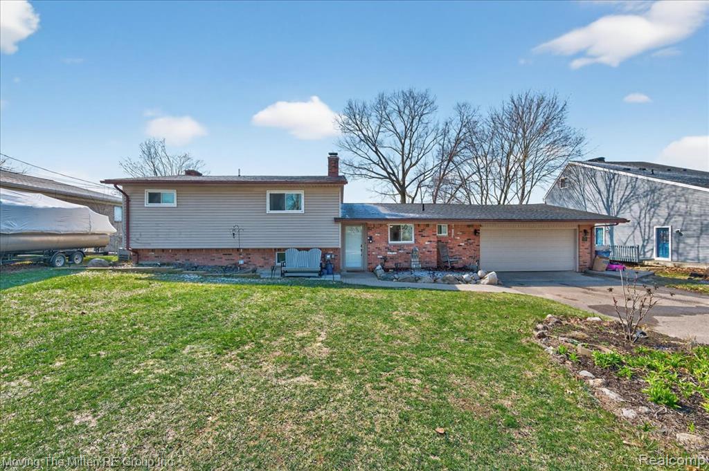 Tri-level home with brick siding, a garage, a chimney, and driveway