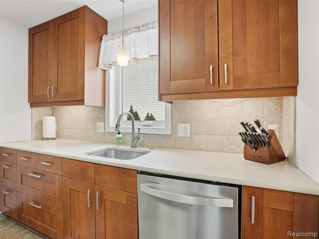Kitchen featuring wood finish cabinets, dishwasher, light stone counters, pendant lighting, and backsplash