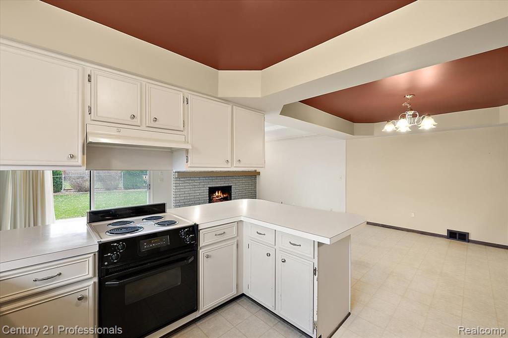 Kitchen with electric range, white cabinets, a peninsula, light countertops, and under cabinet range hood