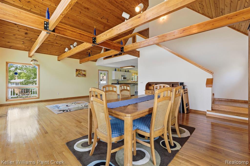 Vaulted wood-paneled ceiling with exposed beams, wood-finish flooring, white walls, and a large window