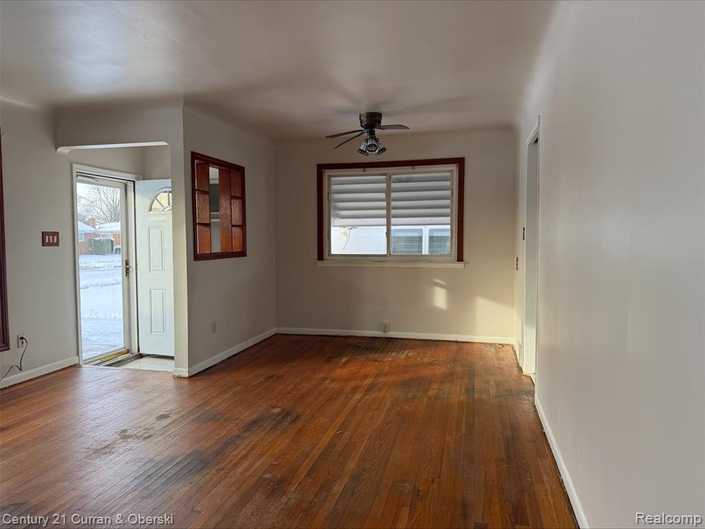 Empty room with ceiling fan, dark wood-style floors, and plenty of natural light