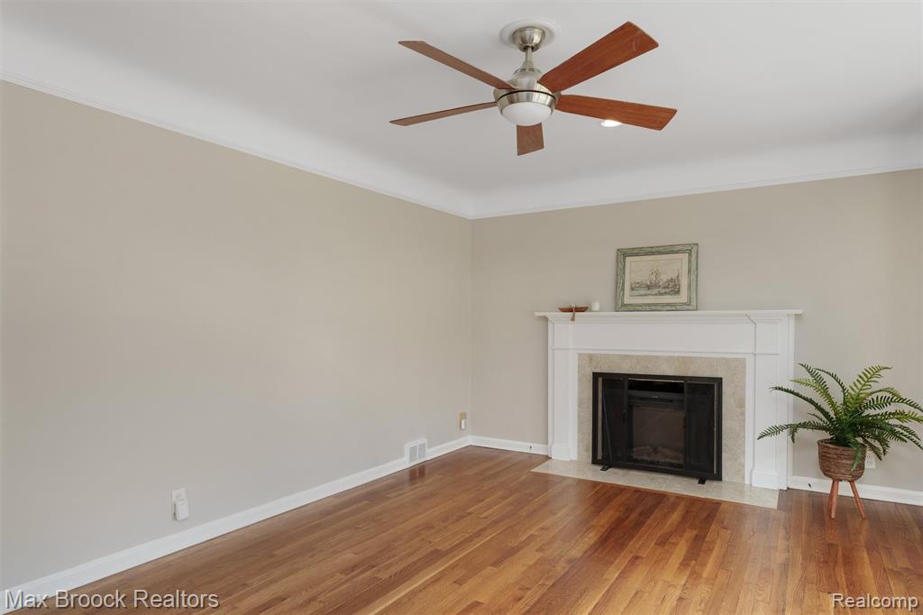 Unfurnished living room featuring wood finished floors, ceiling fan, a fireplace, and crown molding