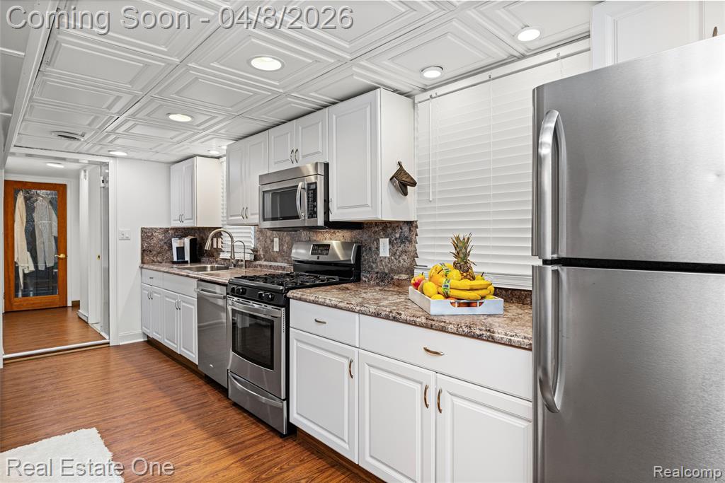 Kitchen featuring stainless steel appliances, white cabinetry, light stone counters, dark wood-style floors, and recessed lighting